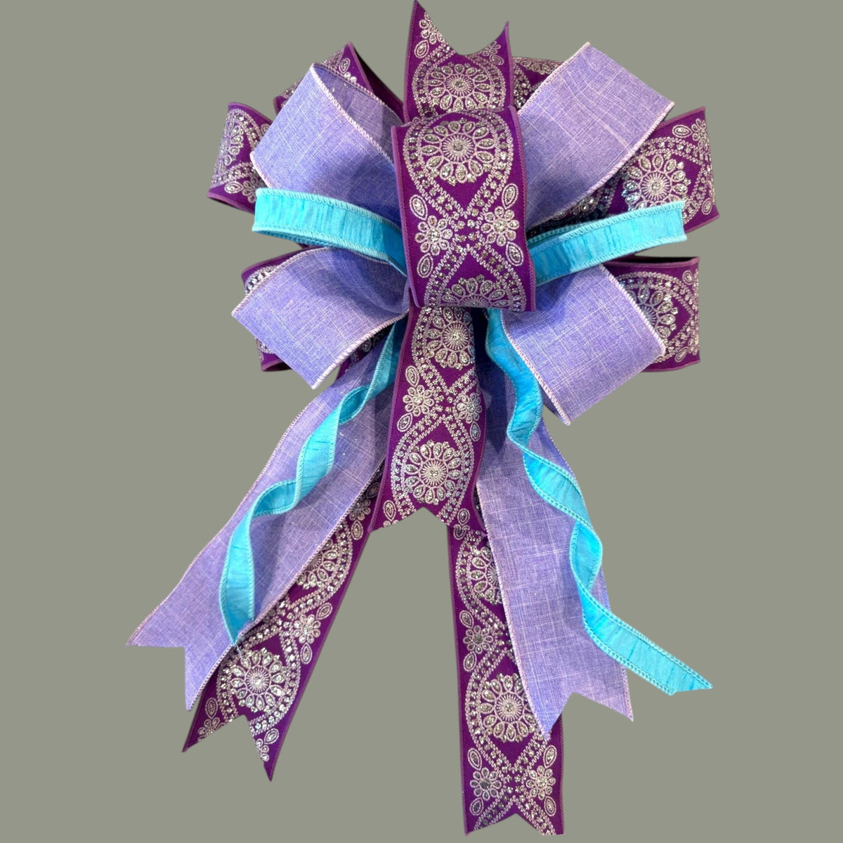 The Matthew John Collective Amethyst Tide wreath bow in purple and turquoise with silver floral ribbon accents.