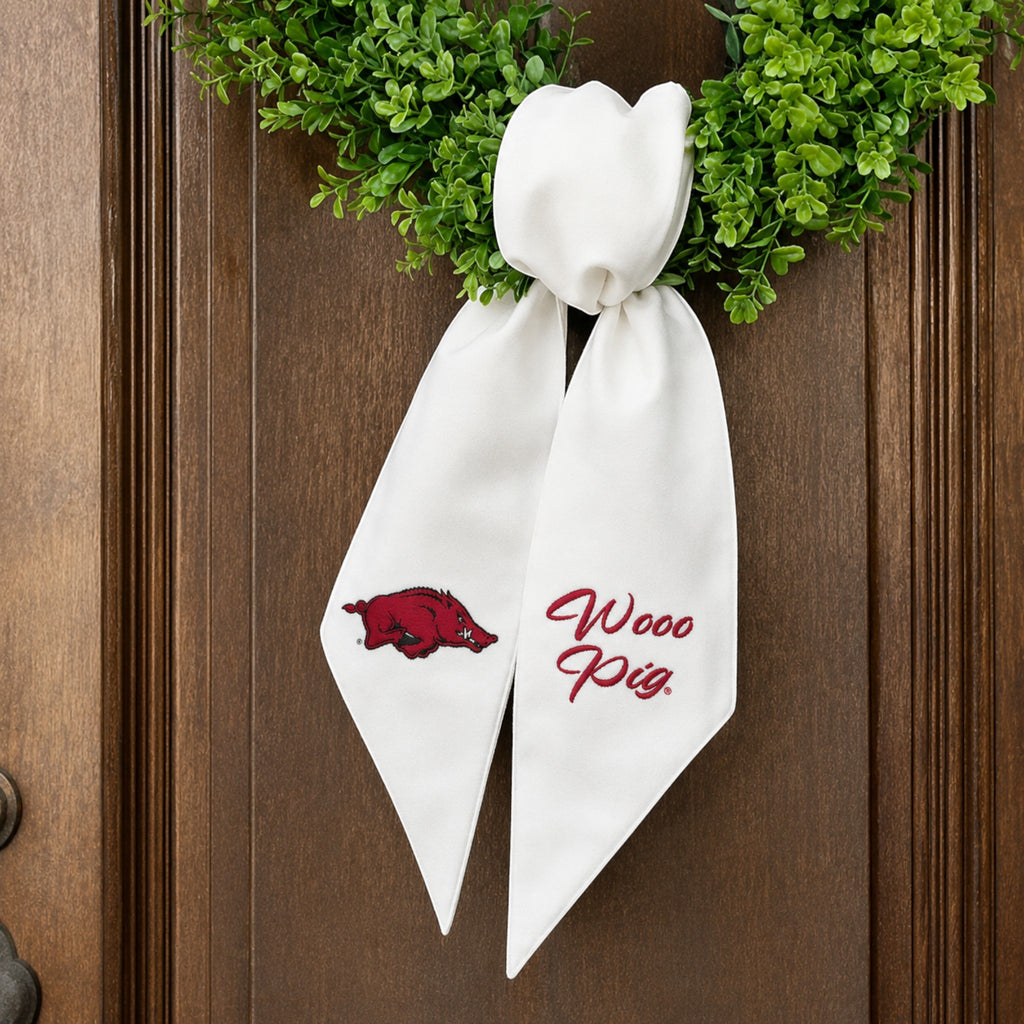 The Matthew John Collective white Arkansas wreath sash with red embroidered Razorback logo and Wooo Pig text.