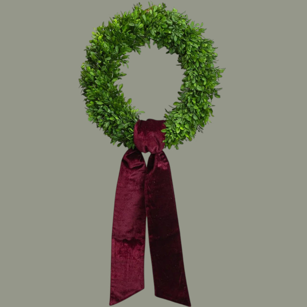 The Matthew John Collective burgundy velvet wreath sash tied on a green boxwood wreath with pointed ends