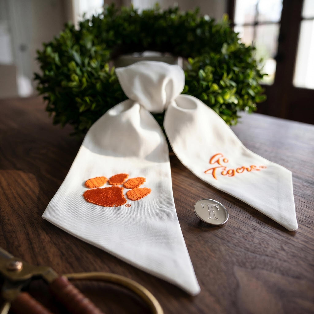 The Matthew John Collective white Clemson wreath sash with orange paw print and Go Tigers embroidery on a green wreath