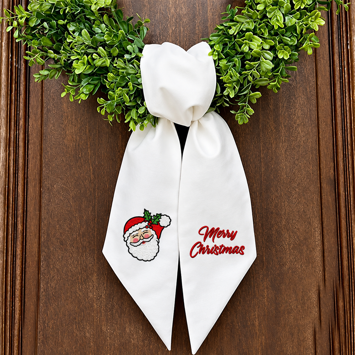 The Matthew John Collective white cotton canvas wreath sash with embroidered Santa and Merry Christmas lettering.