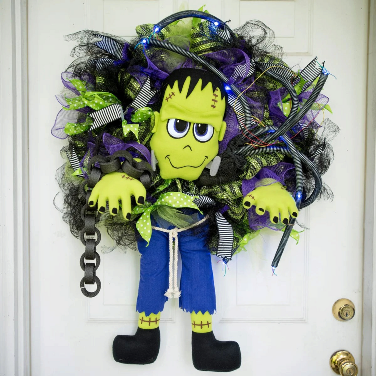 The Matthew John Collective plush Frankenstein monster wreath attachment with green skin and purple pants on a wreath.