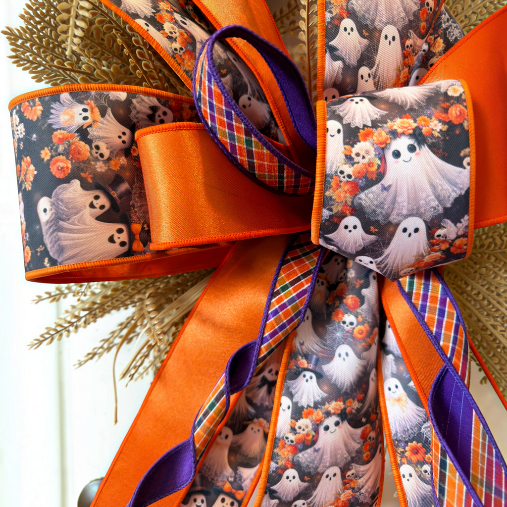 The Matthew John Collective oversized Halloween ghost wreath bow with orange, purple, and plaid ribbon accents.