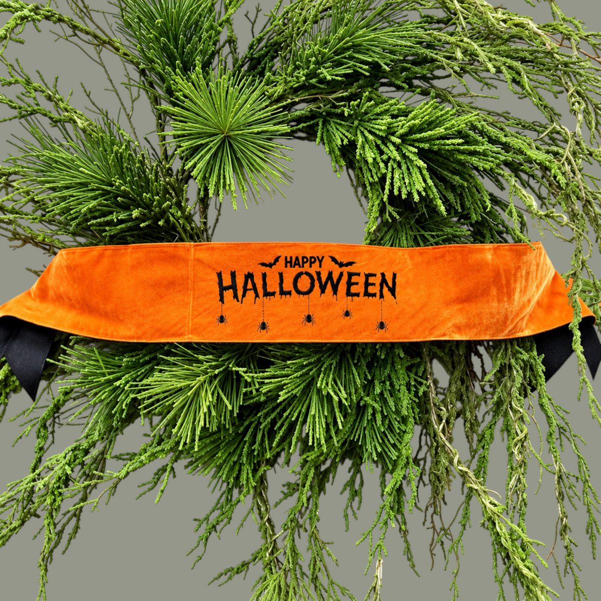 The Matthew John Collective orange satin Happy Halloween wreath banner with black embroidery and dangling spider motifs.