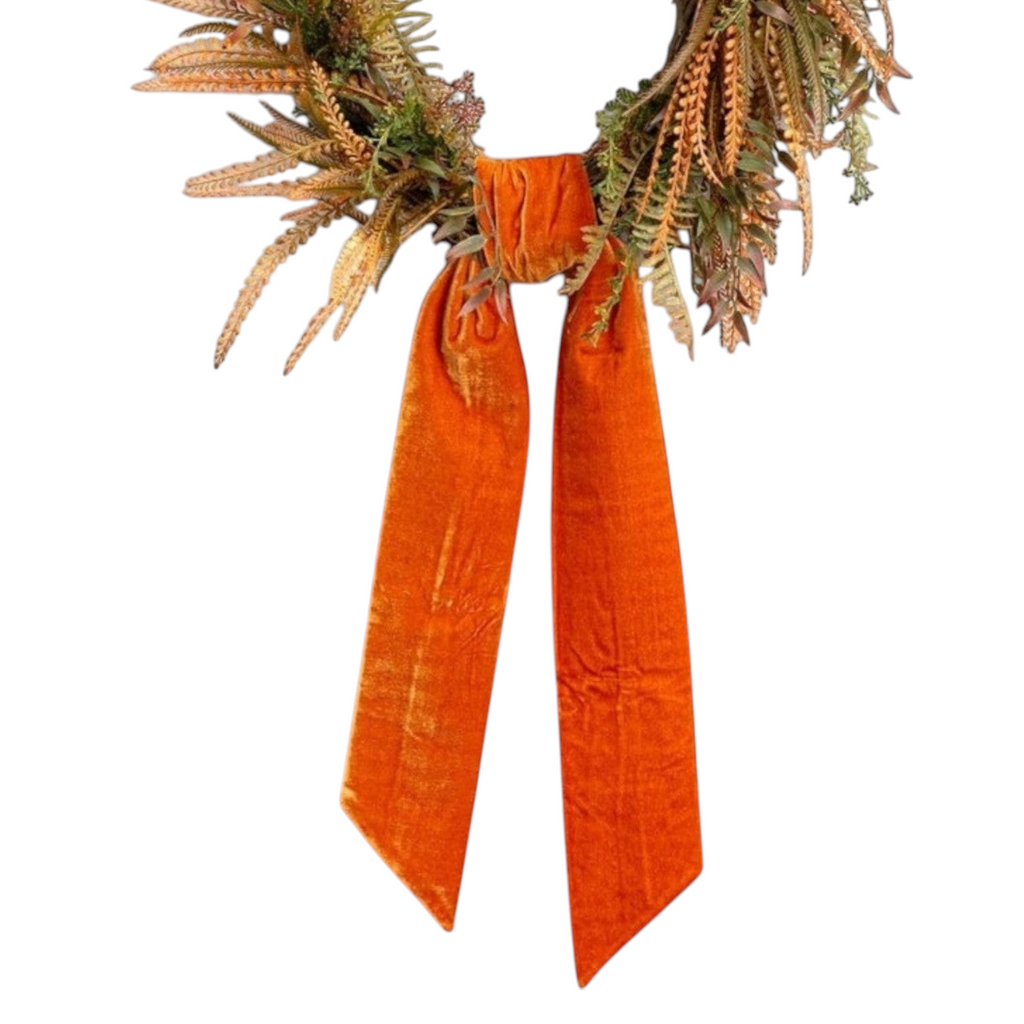 The Matthew John Collective orange velvet wreath sash draped on a fall foliage wreath with pointed tapered ends