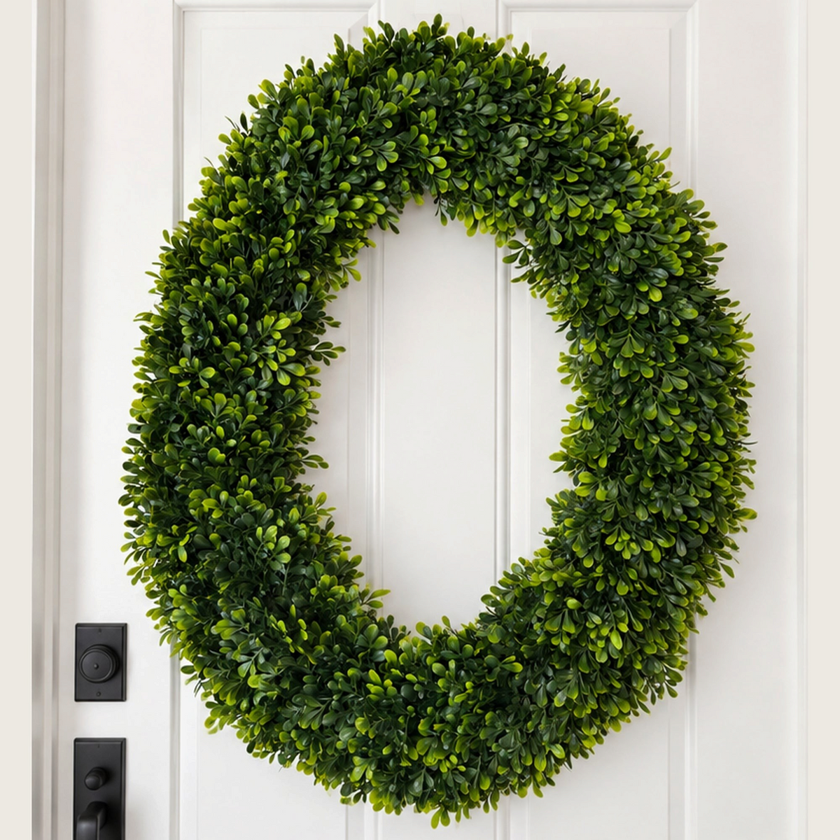 The Matthew John Collective 24x30 inch oval artificial boxwood wreath with lush green foliage on a white front door.
