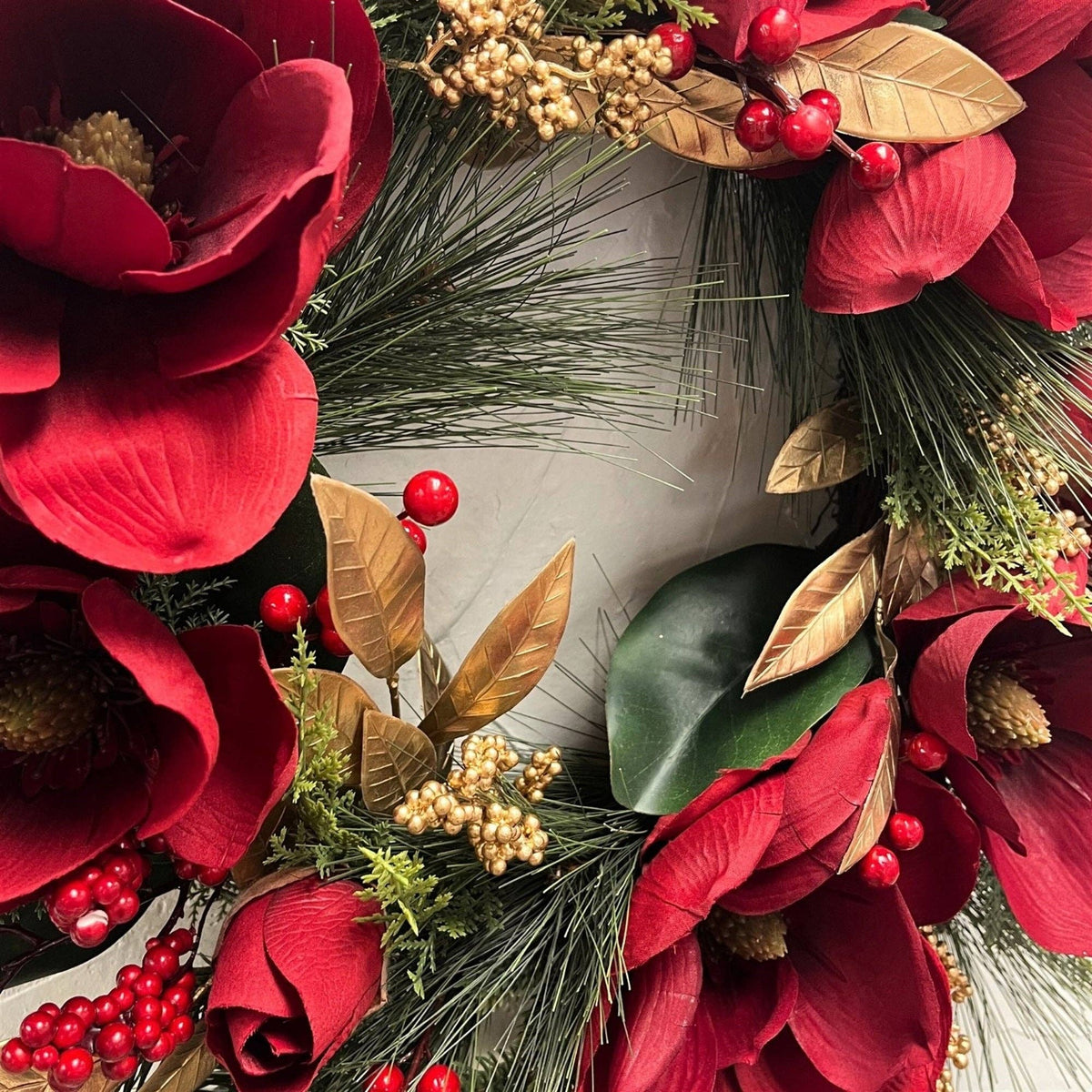 The Matthew John Collective 24-inch Christmas wreath with red magnolia blooms, gold leaves, berries, and pine needles.