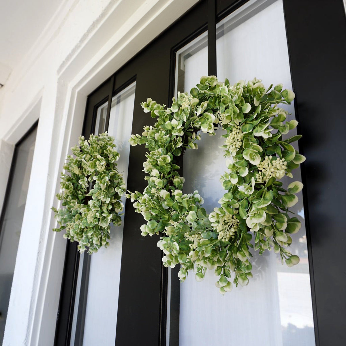 The Matthew John Collective 20-inch seeded eucalyptus wreath with white floral accents on a black front door