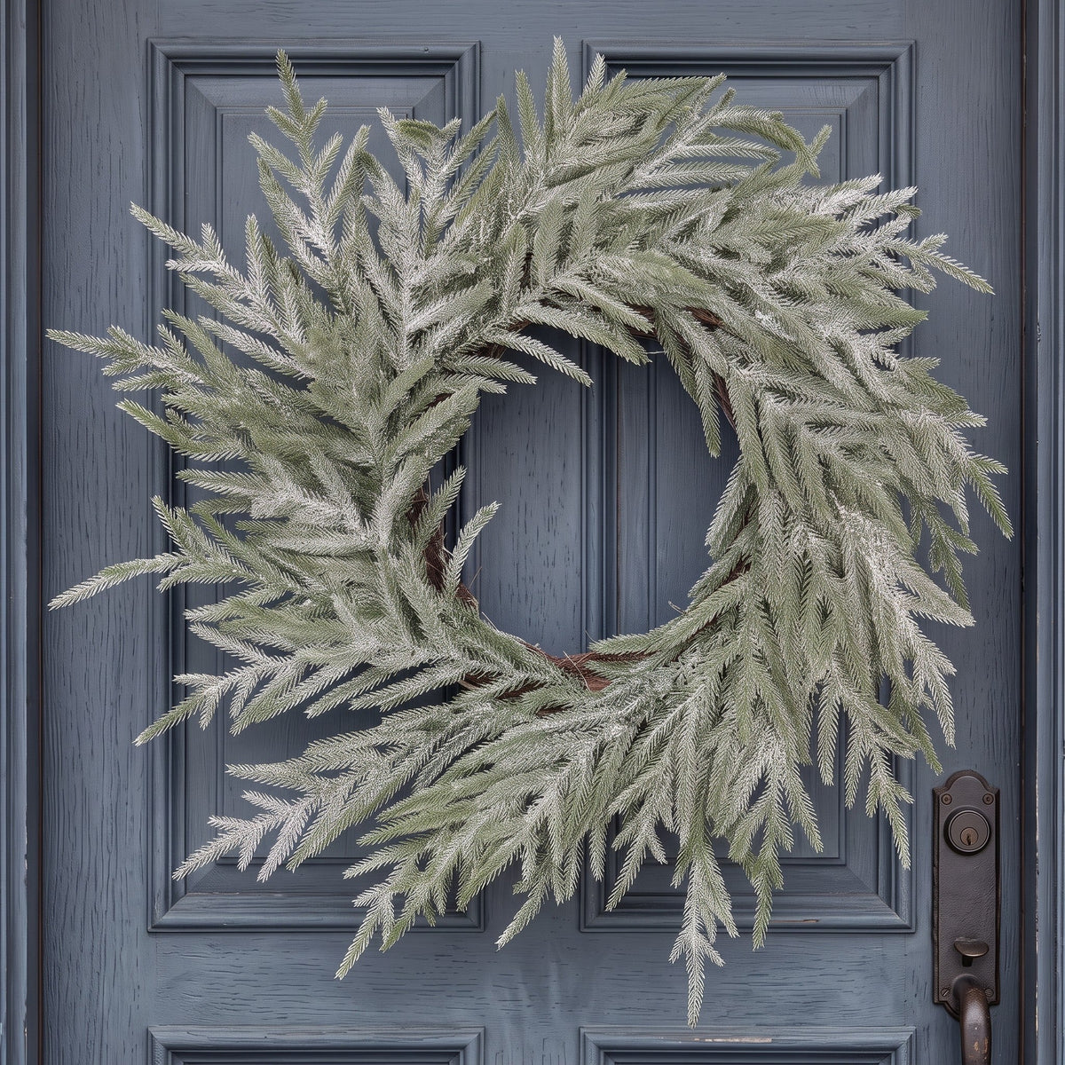 The Matthew John Collective 22-inch snowy Norfolk pine wreath with realistic flocked needles on a blue front door.
