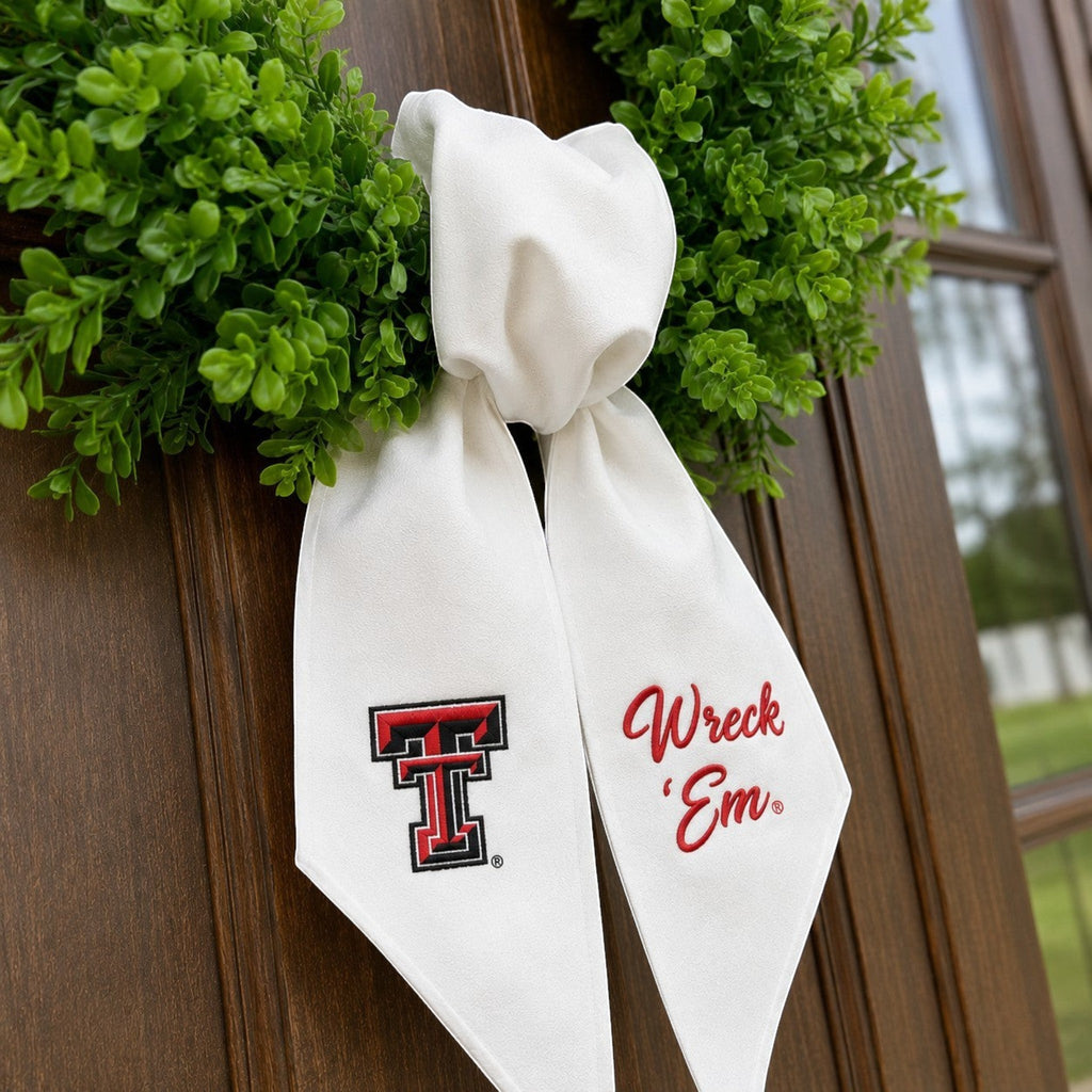 The Matthew John Collective white Texas Tech wreath sash with embroidered team logo and Wreck Em text on a door