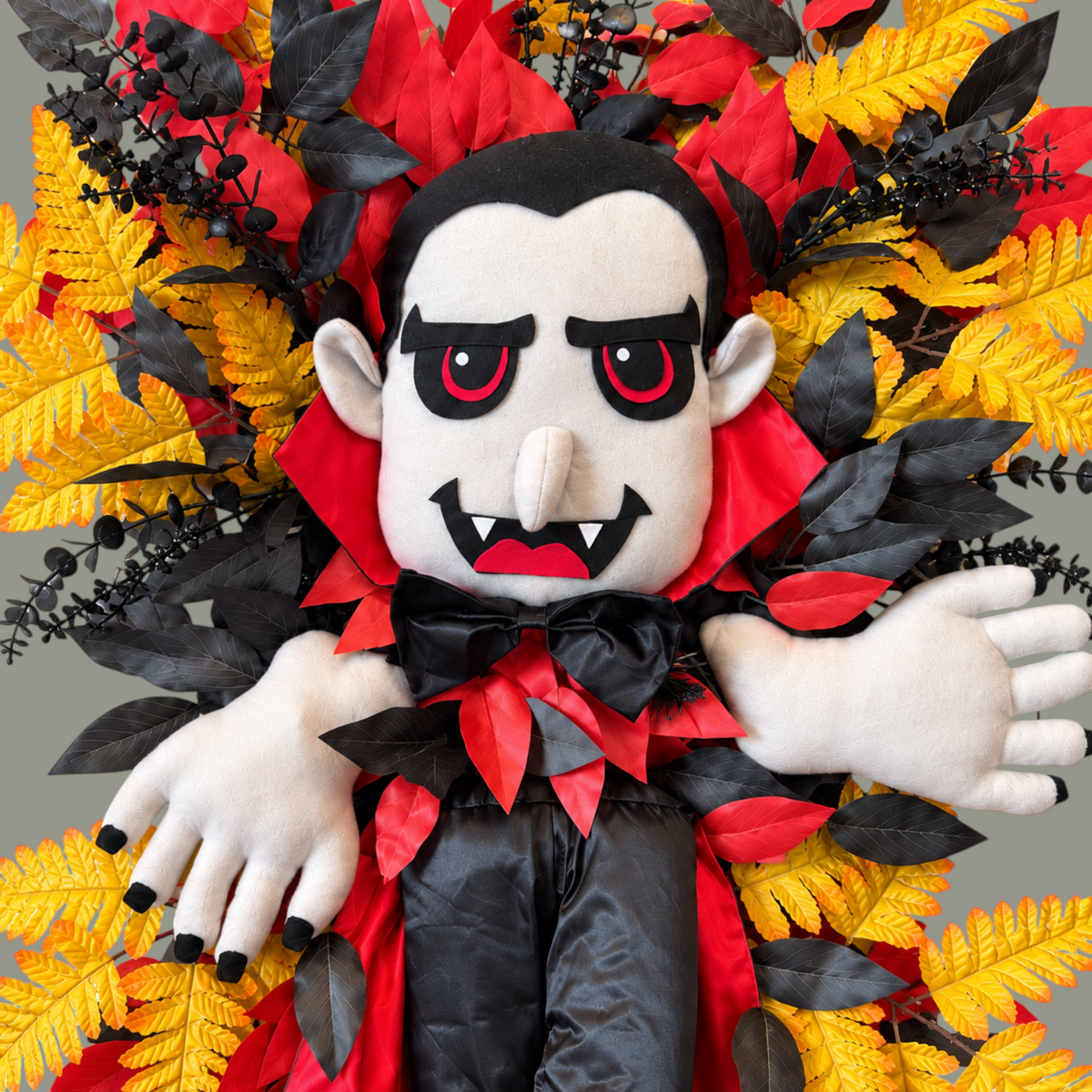 The Matthew John Collective vampire Halloween wreath with plush character, black and red cape, and autumn foliage.