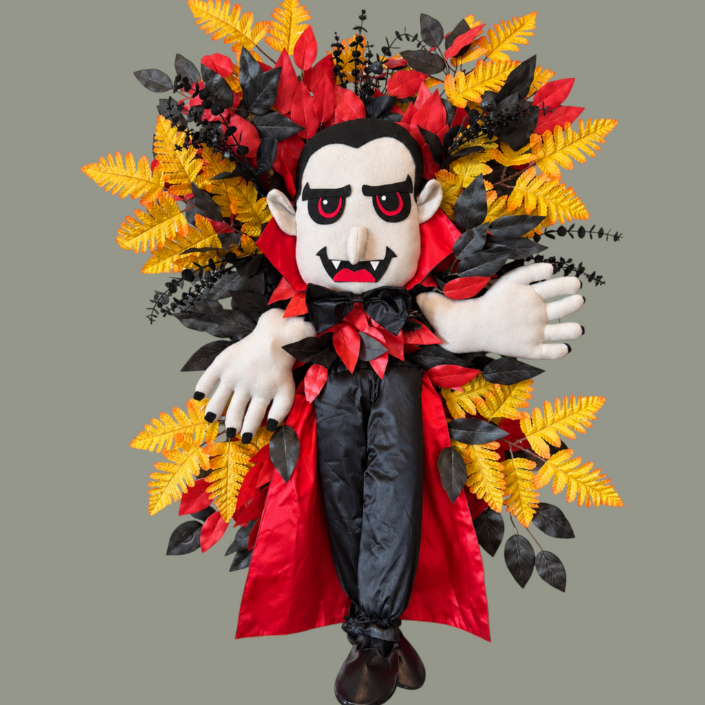 The Matthew John Collective vampire Halloween wreath with plush figure, red and black foliage, and golden fern sprays.
