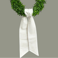 The Matthew John Collective winter white velvet wreath sash tied on a lush green boxwood wreath with pointed ends.