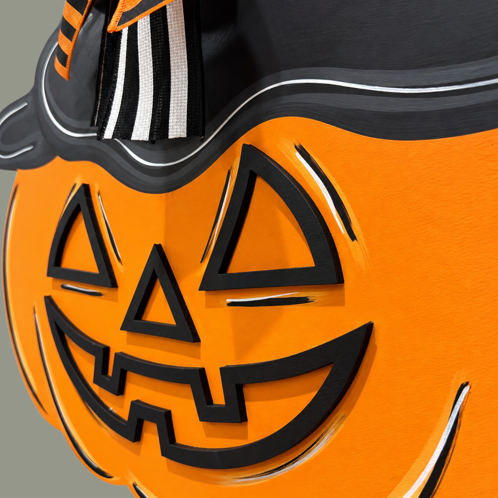 The Matthew John Collective hand-painted wooden jack-o-lantern door hanger with a witch hat and striped bow